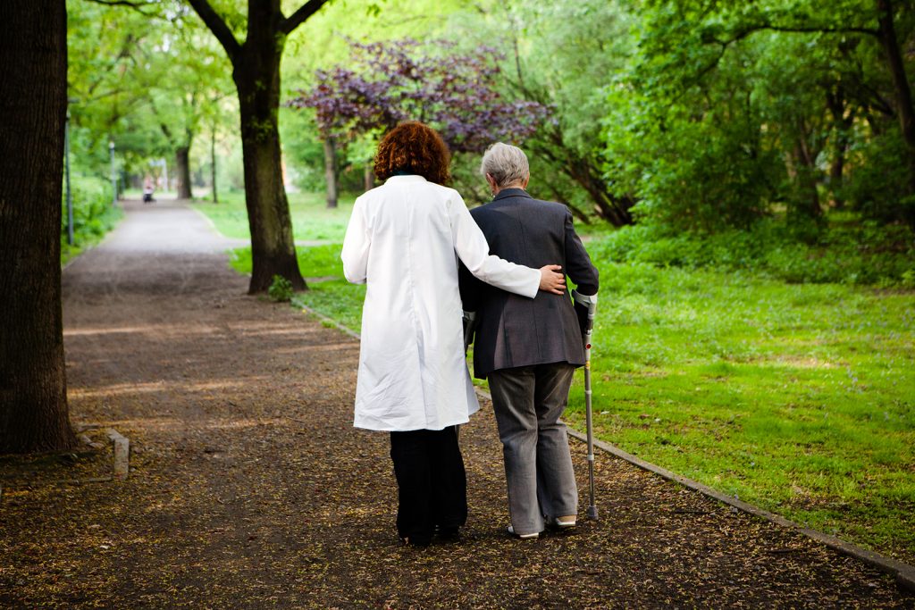 Healthcare Worker helps senior lady by walking on crutches